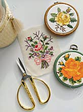 Vintage wooden embroidery hoops, scissors, needle, thread and fabric with floral cross-stitch embroidery on white