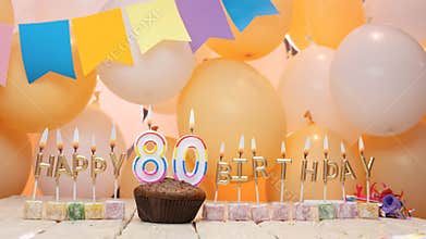 Happy birthday greetings for 80 years from gold letters of candles burning against the background of mine space balloons.