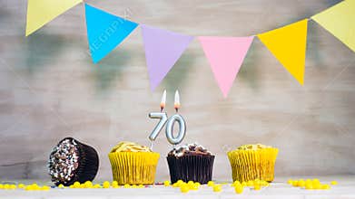 Birthday background with number 70. Beautiful birthday card with colorful garlands, a muffin with a candle burning copyspace.