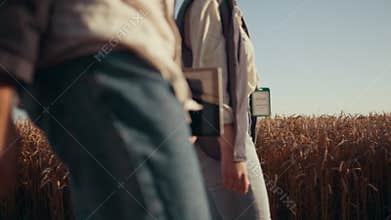 Farm workers walk wheat farmland. Unknown agronomist hands hold tablet closeup.