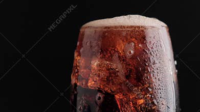 Soda fizzy cold drink in a glass with ice cubes close-up on a black background.