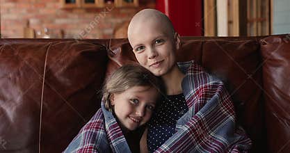 Female cancer patient her little daughter resting on sofa indoor