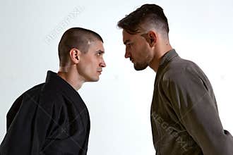 Guys in kimono standing in stance face to face before karate fight workout on white studio backdrop, close up portrait