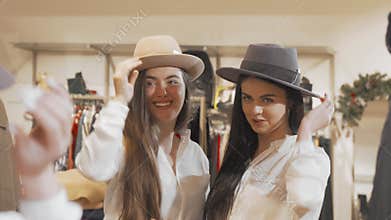 Female friends having fun at clothing store trying hats together
