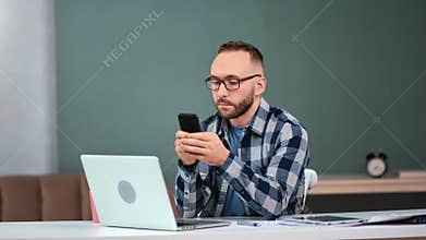 Focused business male chatting use smartphone sitting at modern workplace. Medium shot on RED camera