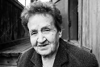 Portrait of old woman near a rural house. Black and white photo.