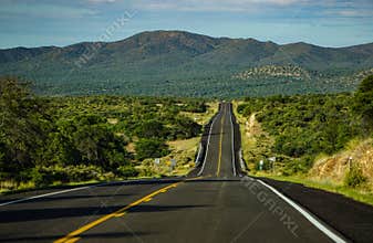 A straight expanse of highway on New Mexico state route 90, through high country of mountains, under a summer sky