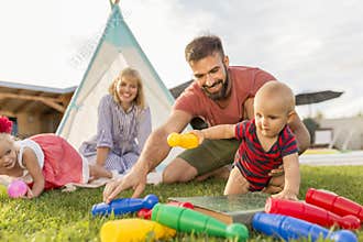 Parents having fun playing bowling with little children while camping in the backyard
