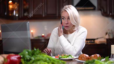 Hurrying young woman eating dinner, surfing Internet on laptop, and talking on the phone. Portrait of modern Caucasian