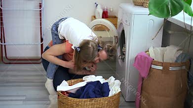 Mom and daughter have fun when doing laundry domestic chore. Child play with mom, jump