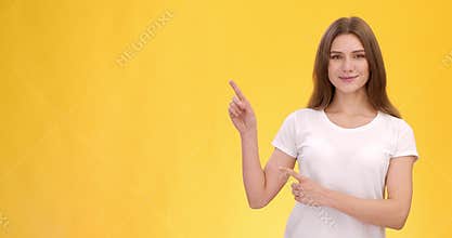 Young cheerful lady pointing aside at copy space over orange studio background, free space for text or mockup