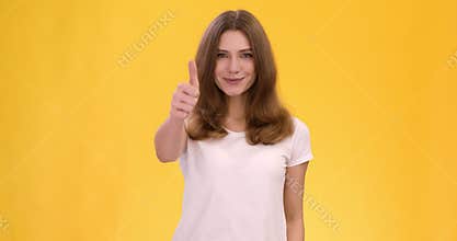Cheerful confident lady gesturing thumb up, showing like and approval gesture, orange studio background, slow motion