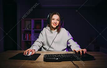 Happy girl gamer in a headset sits at home at the computer and plays video games with a smile on his face and spends a stream