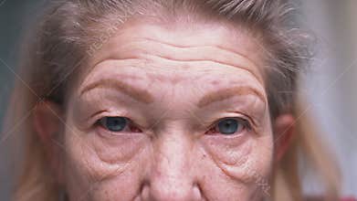 Close up on blue eyes of an elderly woman with wrinkled skin. Depression at old age