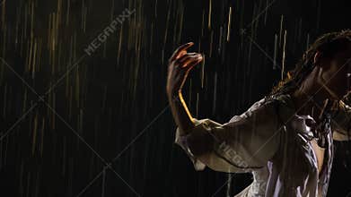Wet young woman in white shirt and beige bodysuit is dancing dramatic modern ballet dance in rain. Ballet dancer moves