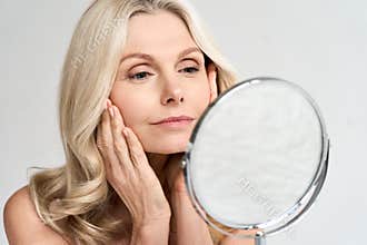 Closeup portrait middle age 50 woman looking at mirror, touching healthy skin.