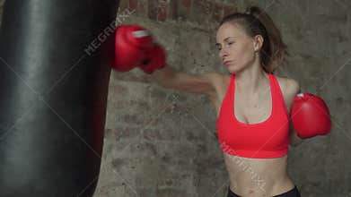 Woman in boxing gloves beats a punch bag. Woman in sportswear, exercising at the gym.