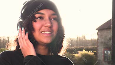 Mixed race African American girl teenager young woman listening to streaming music on headphones backlit by the sun
