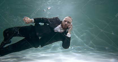 Reaching out to help customers. Young happy businessman in office suit swims underwater talking on the phone slow motion