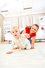 Smiling mommy playing with creeping on floor baby