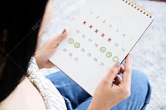 Asian woman hand holding calendar  counting the date and checking her menstrual cycle planning for ovulation
