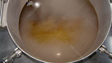 boiling beer wort in big stainless steel reservoir in beer factory