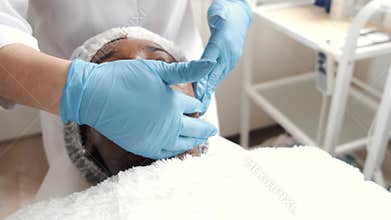 Cosmetologist doing facial massage manually to african client
