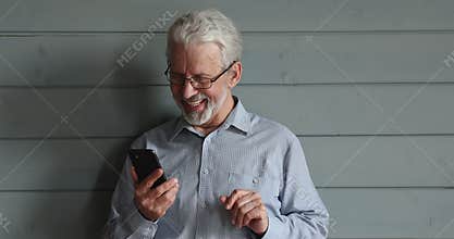 Happy older man in glasses using smartphone.