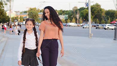Hispanic family young mother single parent holds hand of child daughter schoolgirl walk in city going to school for
