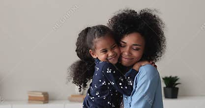 Happy adorable little african kid girl cuddling affectionate young mother.