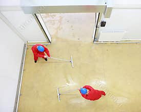 Two workers cleaning floor in industrial building