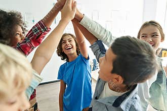 Happy diverse kids school students group giving high five together in classroom.