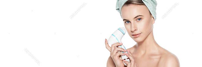 Young woman using sonic facial cleansing brush. Skincare and beauty concept portrait over white. Exfoliation, face massage.