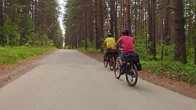 Two young men with backpacks ride bicycles along the road.