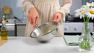 Woman cooking homemade mayonnaise sause whisking ingredients in metal bowl.