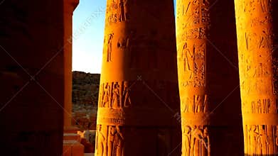 Golden sunlight streaming through ancient stone columns of an Egyptian temple, highlighting intricate carvings and hieroglyphics