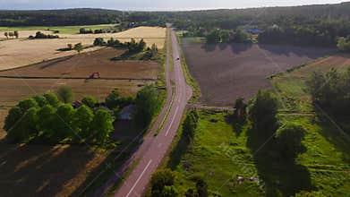 Aerial views showcase a black car driving along a countryside road, surrounded by lush fields and dense forests in