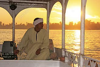Egyptian captain driving his boat on the Nile river at sunset, L