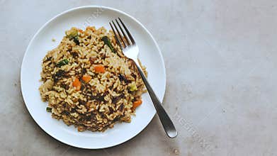 Plate of fried rice with vegetables and meat, fork placed centrally, simple presentation top view