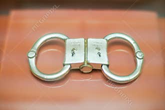 A pair of metallic handcuffs are placed on a light-colored surface, with an adjustable chain linking them together The
