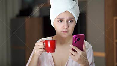 Young cheerful woman with pink smartphone in hands looking to phone screen. Wearing lace pajama. watching a movie on