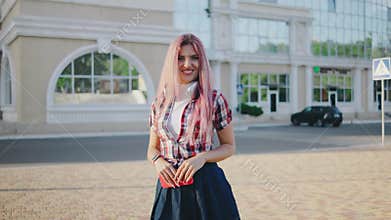 portrait of a young beautiful woman with pink hair on a European street. The girl with headphones looks at the camera