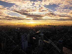 Manila city skyline with skyscrapers and buildings glowing in the golden sunset with clouds and sunbeams. Aerial view of