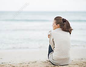 Young woman wrapping in sweater while sitting on lonely beach
