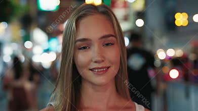 Woman with light smile looks in camera on night city street