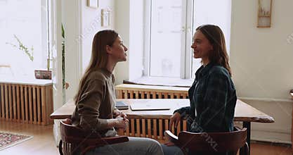 Two happy female colleagues talking in co-working, discussing cooperation