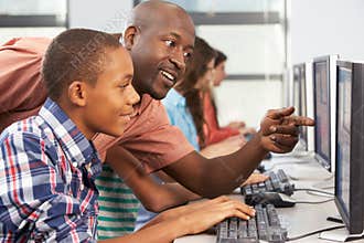 Teacher Helping Students Working At Computers In Classroom