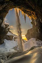 Three mountaineering tourists in front of the frozen Kvernufoss waterfall, with snow and stalagmites and falling water illuminated