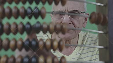 Older man in glasses is calculating with wooden vintage abacus standing behind it