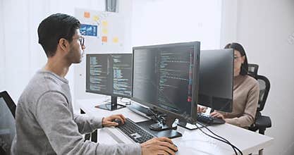 Young adult Asian male, female software developer coding program on desktop computer. Man, woman work from home